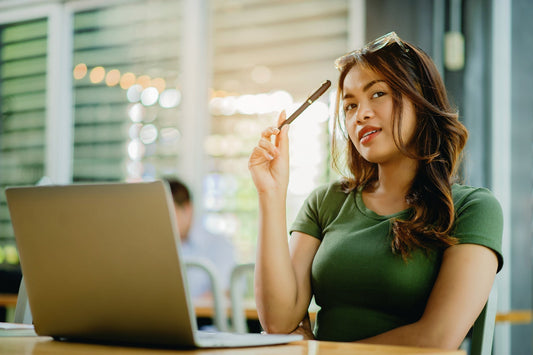 Woman in green shirt holding a pen sits and thinks at her laptop